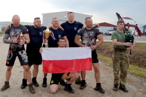 Polscy policjanci stoją z biało-czerwoną flagą. Po prawej stronie stoi szkocki żołnierz i gra na kobzie.