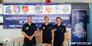 dwóch mężczyzn i kobieta w strojach sportowych na tle baneru Mistrzostwa Polski Policjantów w Tenisie Stołowym