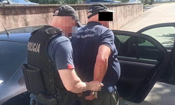 zatrzymany wsiada do nieoznakowanego radiowozu. Obok stoi policjant