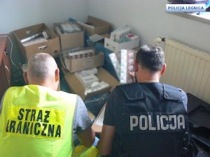 policjant wraz z funkcjonariuszem straży sprawdzają kartony z papierosami