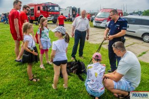 Kilkoro dzieci i dorosłych wokół Przewodnika wraz z jego psem Policyjnym