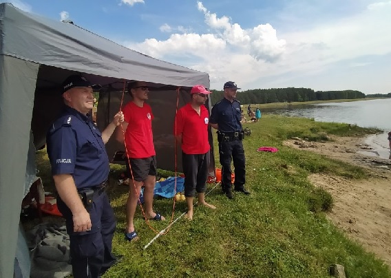 Policjanci oraz Ratownicy WOPR stojący obok namiotu