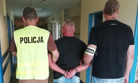 dwaj policjanci , jeden w kamizelce odblaskowej z napisem policja prowadzą zatrzymanego&quot;&gt;