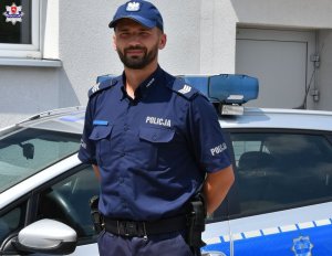 sierżant  sztabowy  Sebastian Janicki stoi obok radiowozu policyjnego