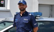 sierżant  sztabowy  Sebastian Janicki stoi obok radiowozu policyjnego
