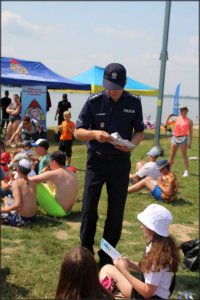 policjant rozdający grupie dzieci ulotki i broszury z zasadami bezpiecznego zachowania nad wodą