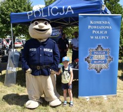 chłopiec trzyma za rękę maskotkę policyjną obok stoi baner Komendy Powiatowej Policji w Słupcy