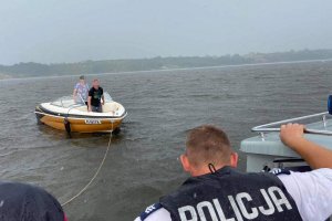 Policjant stoi na łodzi, a za nimi płynie holowana motorówka