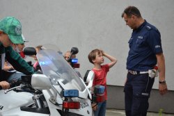 policjant rozmawiający z grupką dzieci obok chłopiec siedzący na motocyklu policyjnym