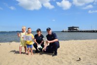 para policjantów na plaży obok dwójka dzieci trzymających w rękach kartkę z logo akcji &quot;Kręci mnie bezpieczeństwo nad wodą&quot;