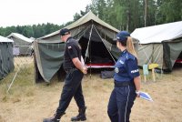 na leśnej polanie policjantka i strażak przechodzą obok namiotów harcerskich