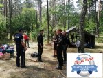 na leśnej polanie policjant i strażacy rozmawiają z harcerzami w prawym dolnym rogu logo akcji koło ratunkowe na białym tle