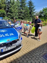 radiowóz policyjny obok grupka dzieci słuchająca policjanta