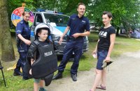 chłopiec ubrany w policyjną kamizelkę kuloodporną i kask obok jego opiekun za nimi w tle para policjantów