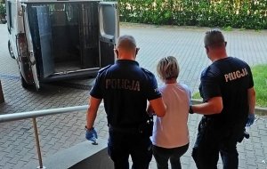 umundurowani policjanci prowadzą zatrzymaną kobietę do policyjnego radiowozu