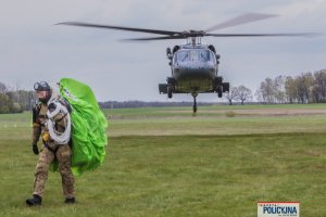 funkcjonariusz BOA idzie ze spadochronem na ramieniu, w tle śmigłowiec policyjny