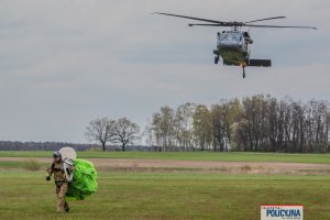 funkcjonariusz BOA idzie ze spadochronem na ramieniu, w tle śmigłowiec policyjny