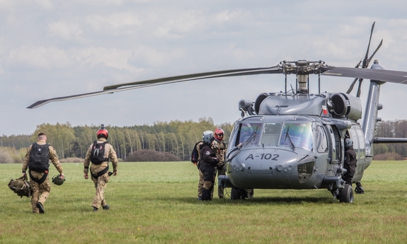śmigłowiec stoi na trawiastym lotnisku, w jego kierunku idą trzej funkcjonariusze &quot;BOA&quot;