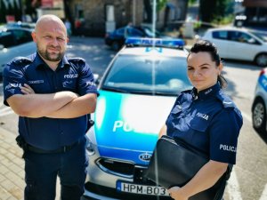 policjant i policjantka stoją przed radiowozem policyjnym