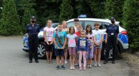 dzieci pozują z policjantem do zdjęcia na tle radiowozu