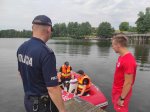 policjant i ratownik stoją na pomoście obok w pontonie na wodzie w kamizelkach ratunkowych siedzą inni dwaj policjanci