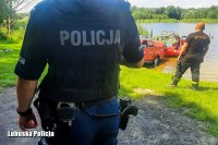 policjant z ratownikiem stoją odwróceni tyłem przy zbiorniku wodnym