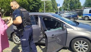 umundurowany policjant z psem na rękach, samochód osobowy z wybitą szybą