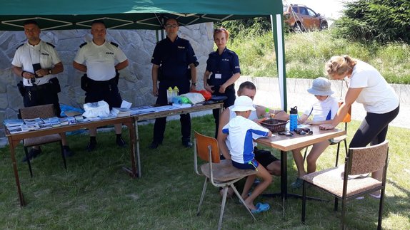 policjanci prezentują na stoisku profilaktycznym ulotki i gadżety promujące bezpieczeństwo