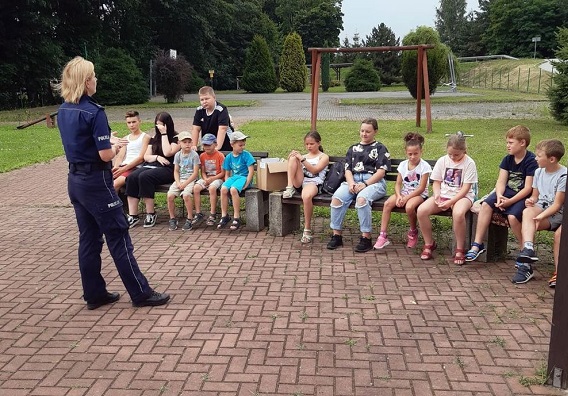 Policjantka podczas rozmowy z dziećmi siedzącymi na ławce