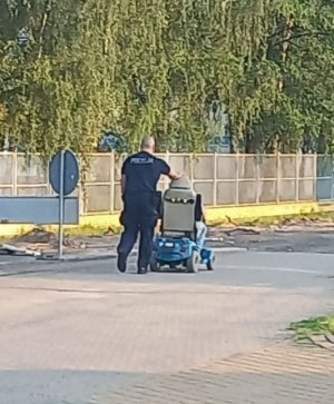 Umundurowany policjant pcha wózek inwalidzki z siedzącą na nim kobietą - widok z tyłu