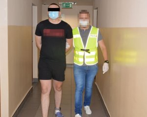 nieumundurowany policjant w żółtej kamizelce z napisem Policja prowadzi zatrzymanego mężczyznę, który ma na sobie czarną koszulkę