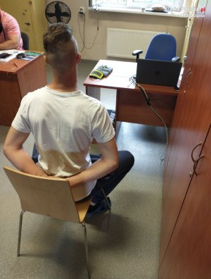 zatrzymany mężczyzna siedzi na krześle podczas przesłuchania, zakute w kajdanki ręce trzyma z tyłu