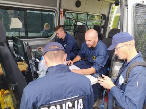 Policjanci z grupy poszukiwawczej odbierają odbiorniki gps od kierującego poszukiwaniami