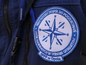 Plakietka na mundurze policjanta. Na niebieskim tle napis Nieetatowy Zespół Do Poszukiwań Osób Zaginionych w Terenie Otwartym SPPP Opole
