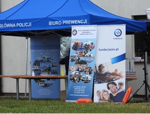 Granatowy namiot z napisem Komenda Główna Policji Biuro Prewencji oraz trzy banery pierwszy od lewej Akcji Kręci mnie bezpieczeństwo nad wodą, drugi Wydział Profilaktyki Społecznej Biura Prewencji KGP z danymi teleadresowymi, trzeci PZU Fundacja.