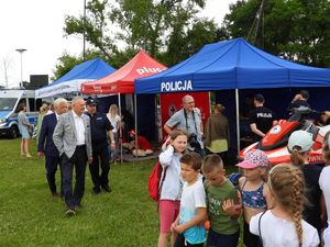Grupa dzieci, cywilnych osób dorosłych, policjantów w mundurach, którzy stoją obok namiotów profilaktycznych Policji i WOPR-u