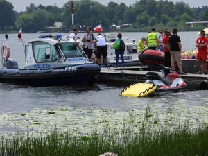 Pomost, na którym stoi grupa ludzi, wokół którego zacumowane są: łódź ratownicza WOPR, skuter WOPR z zaczepioną z tyłu żółtą deską ratowniczą, dwa pontony Policyjne.