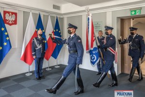 poczet sztandarowy wchodzi do sali, w głębi stoi Komendant Główny Policji