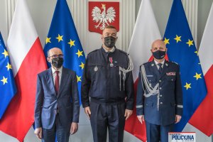 Komendant Główny, Francuski Zastępca Attaché ds. Bezpieczeństwa Wewnętrznego oraz mężczyzna stoją na tle flag Polski i Unii Europejskiej, u góry na ścianie wisi godło Polski