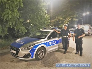 nocna pora, dwaj policjanci stoją obok radiowozu, w tle widać drzewa