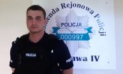 sierż. Maciej Krassowski stoi na tle ściany z logiem Komendy Rejonowej Policji Warszawa IV