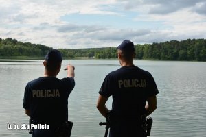 policjanci stoją tyłem na tle jeziora
