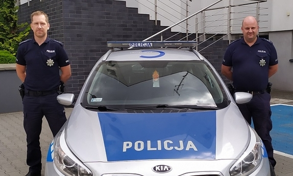 dwaj policjanci stoją obok radiowozu policyjnego