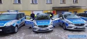 trzy radiowozy policyjne , obok jednego z nich stoja dwaj policjanci