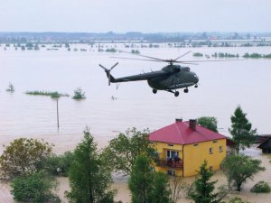 Mi-8 w akcji ratowniczej podczas powodzi leci nad zalanymi terenami i budynkiem zalanym wodą.