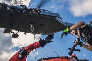 Strażacy napełniają bambi bucket, nad nimi unosi się śmigłowiec.