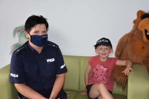 Policjantka z dziewczynką  w Niebieskim pokoju. Dziewczynka ma założoną na głowie czapkę z napisem Policja
