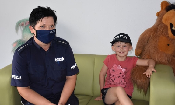 Policjantka z dziewczynką  w Niebieskim pokoju. Dziewczynka ma założoną na głowie czapkę z napisem Policja