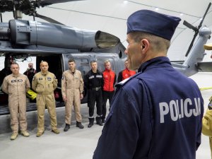 Przemówienie zastępcy Komendanta Głównego Policji nadinsp. Romana Kustera do członków ekipy wyruszającej do Turcji, stojących na tle śmigłowca Black Hawk.