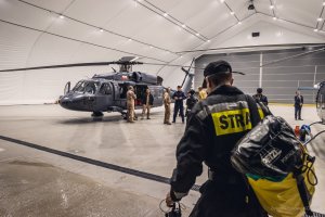 Strażak z plecakiem idzie do śmigłowca S70i Black Hawk, przy którym widoczna jest jego załoga.